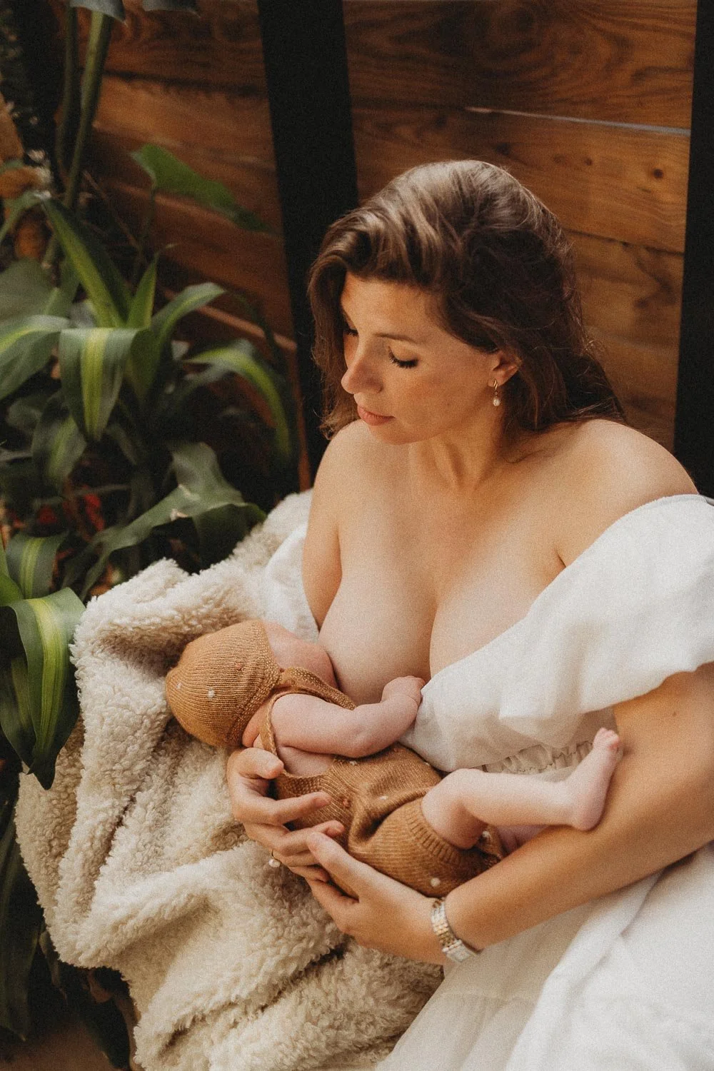 Mother breastfeeding her newborn, wrapped in a cream blanket, during an in-home newborn session in Dorval, Montreal