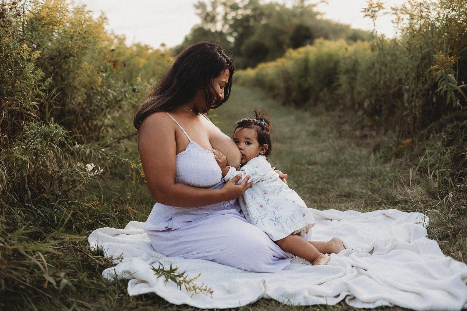 Mom breastfeeding her baby daughter at nature, baby is looking at the camera and mom looking at baby, captured during a motherhood photoshoot in Boucherville Islands, Montreal