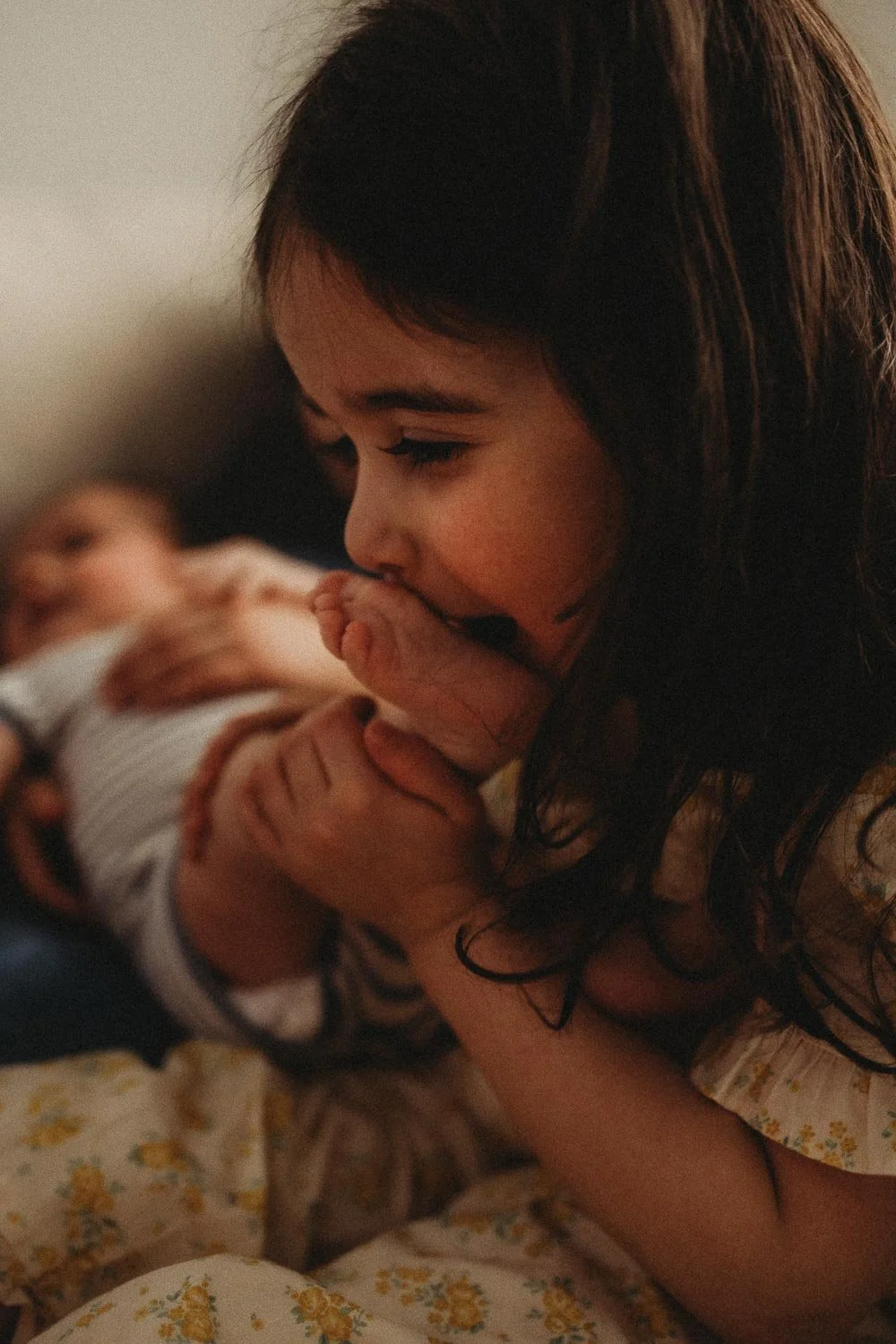 Sister kissing and tickling her baby brother's foot while an in-home newborn photoshoot in Montreal