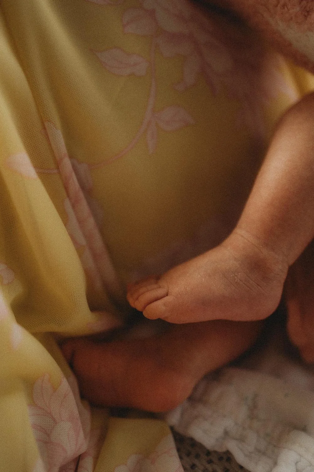 Close-up of a newborn baby's hand gently gripping a person's finger with floral-patterned yellow fabric nearby captured during an in-home newborn photo session at Dollard-Des Ormeaux, Montreal