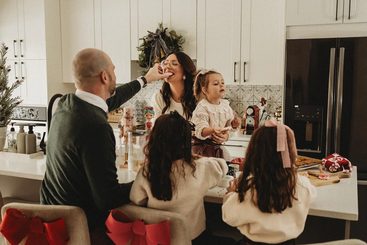 Dad feeding mom cookies while their three daughters are decorating cookies, captures during an in-home family photoshoot in Montreal