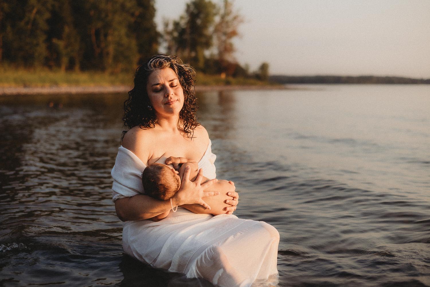 Woman breastfeeding her naked baby with closed eyes, while enjoying her moment, captured during an outdoor Motherhood Photoshoot at Cap-Saint-Jacques, Montreal