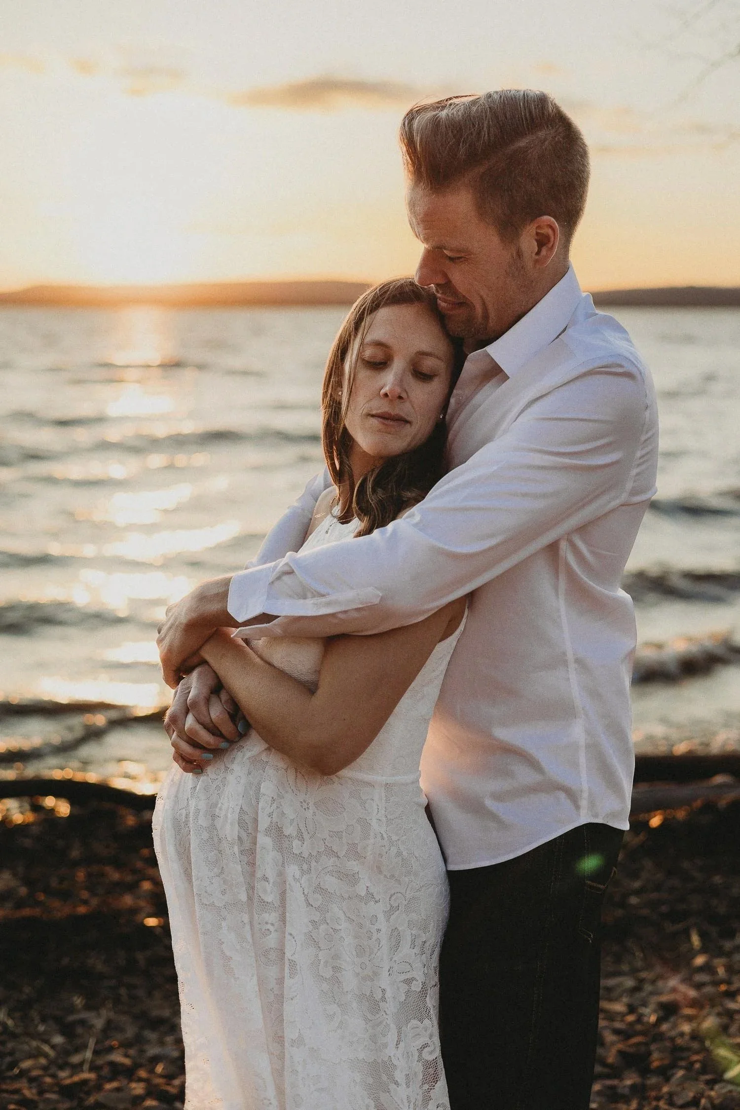 Pregnant woman and husband hugging tenderly with closed eyes, captured during an outdoor beach maternity photoshoot in Cap-Saint-Jacques, Montreal