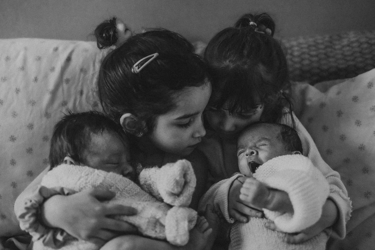 Two sisters holding and cuddling their twin sibling babies at an in-home newborn photo session in La Salle, Montreal