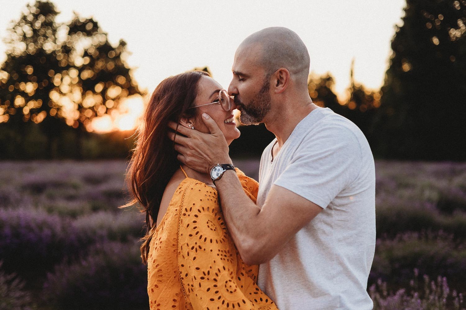 A couple sharing an intimate moment outdoors during sunset, with trees and lavender flowers in the background during an outdoor Family Photo session at La Maison Lavande, Quebec