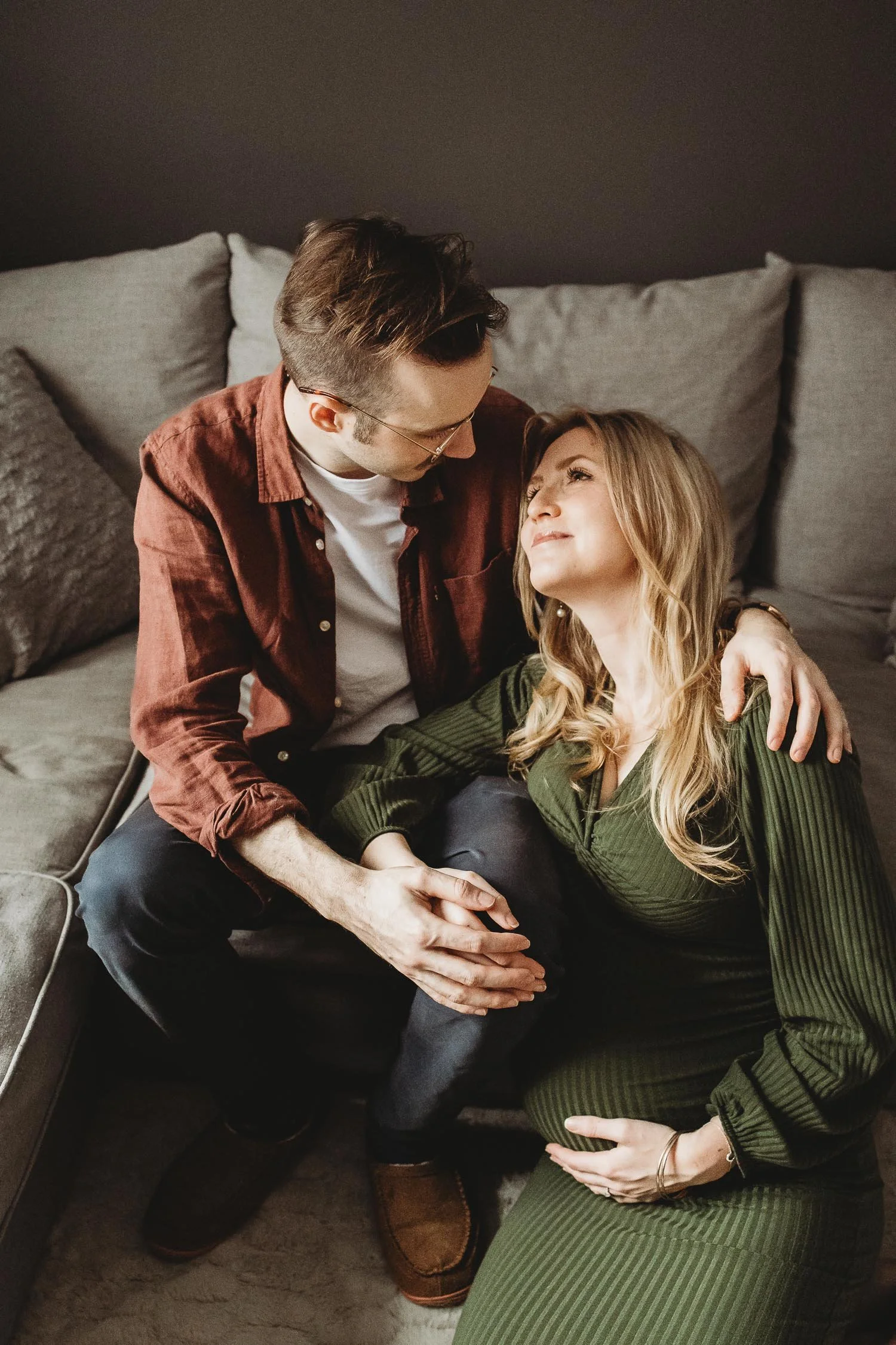 A man and woman sitting on a couch, the man comforting the pregnant woman by holding her hand and shoulder, with a dark background.