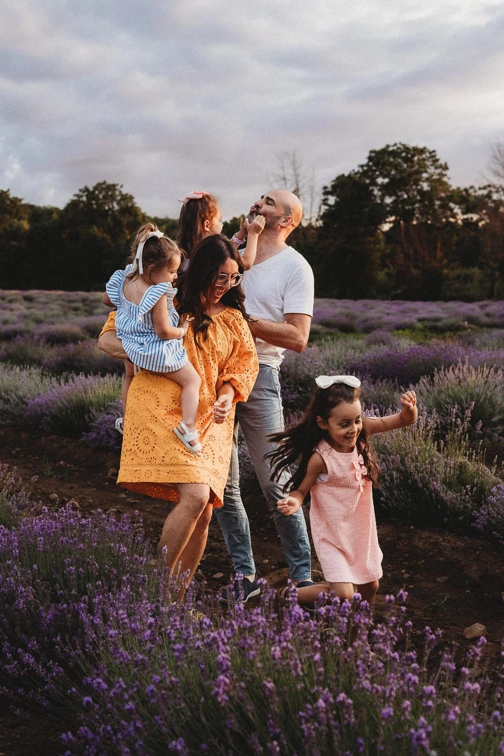 Family of five enjoying a lavender field at sunset, playing, laughing, and hugging each other captured during a golden hour family photo session at La Maison Lavande