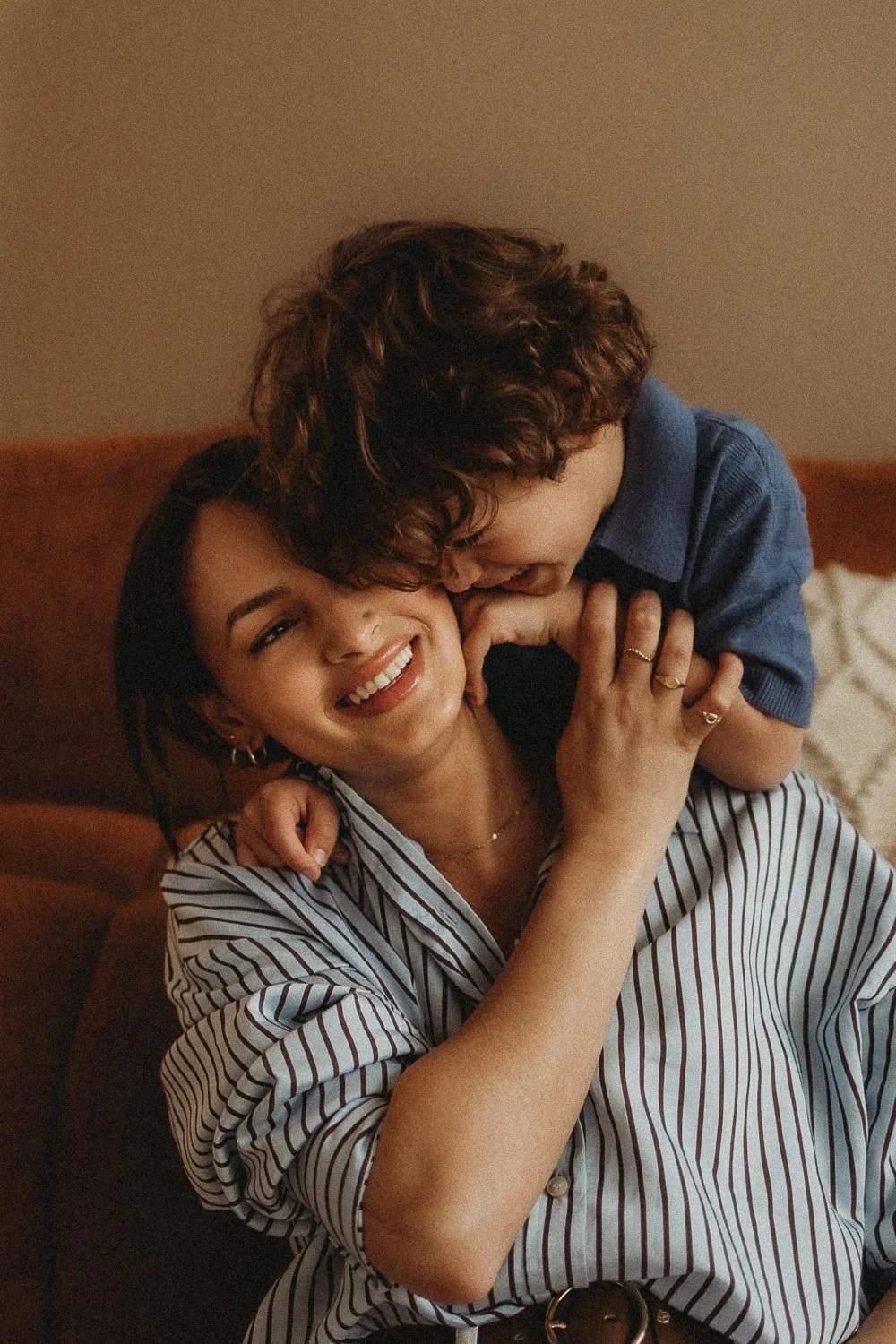 An in-home motherhood photo session in Montreal portraying a mom and a young boy sharing a joyful moment, with the boy kissing her on the cheek and the woman smiling.