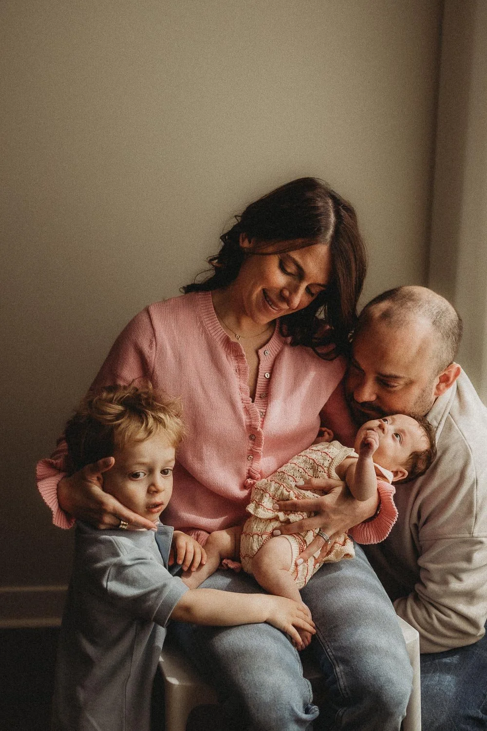 A woman and a man lovingly hold two young children in a tender family moment during an in-home newborn photoshoot in Hampstead, Montreal