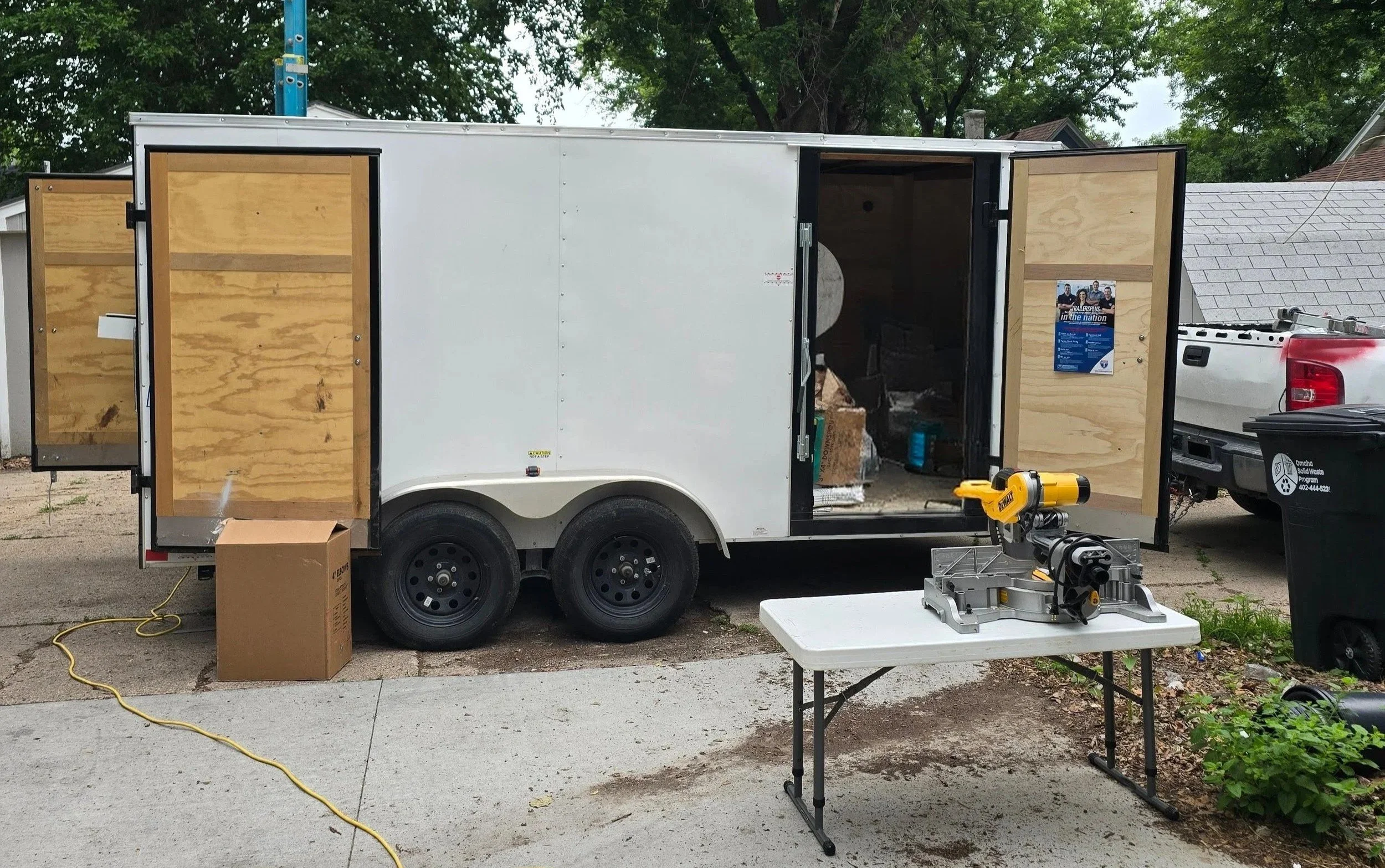 Contractor work trailer open and equipped with tools and materials for home exterior repairs, showing an organized job site setup.