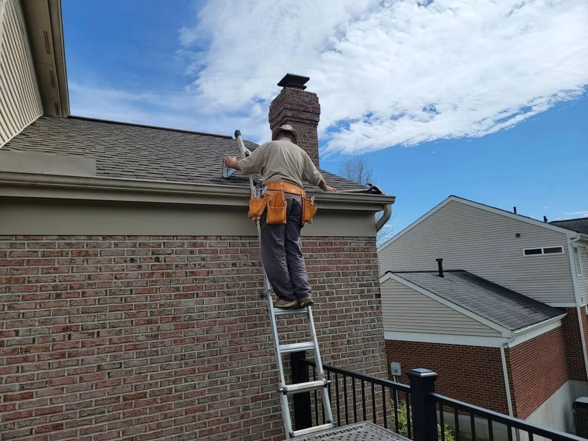 Omaha contractor preparing a roof and gutter repair on a brick house with ladder and toolbelt