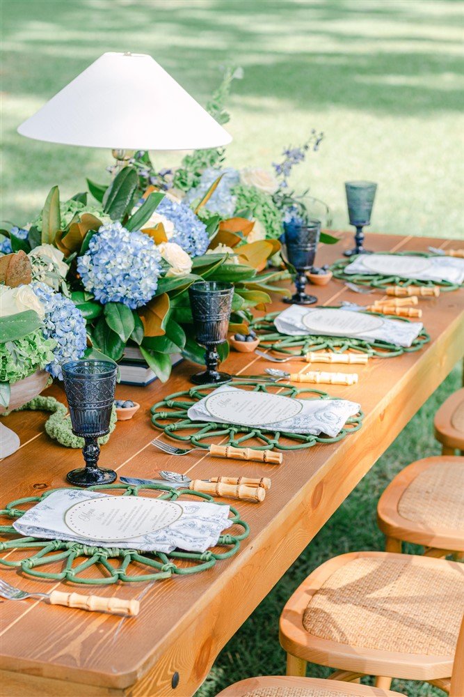A tablescape set with our Farmhouse Table, Bamboo Flatware, Georgia Napkins, Skidaway Island Chairs, Whitaker Lamps, Vintage Blue Goblets, and Camdyn Chargers.