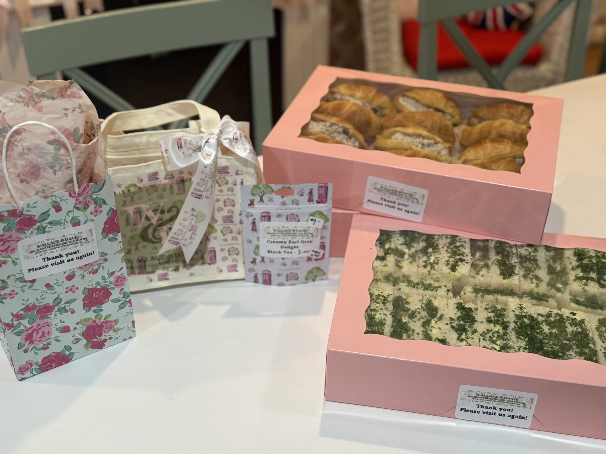 Gift bags with floral and striped patterns, two pink boxes with clear windows showing baked goods, possibly scones and cookies, on a white table.