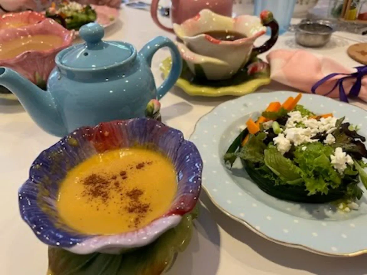 Colorful ceramic teapots and bowls on a table, with a plate of salad and a bowl of soup or sauce