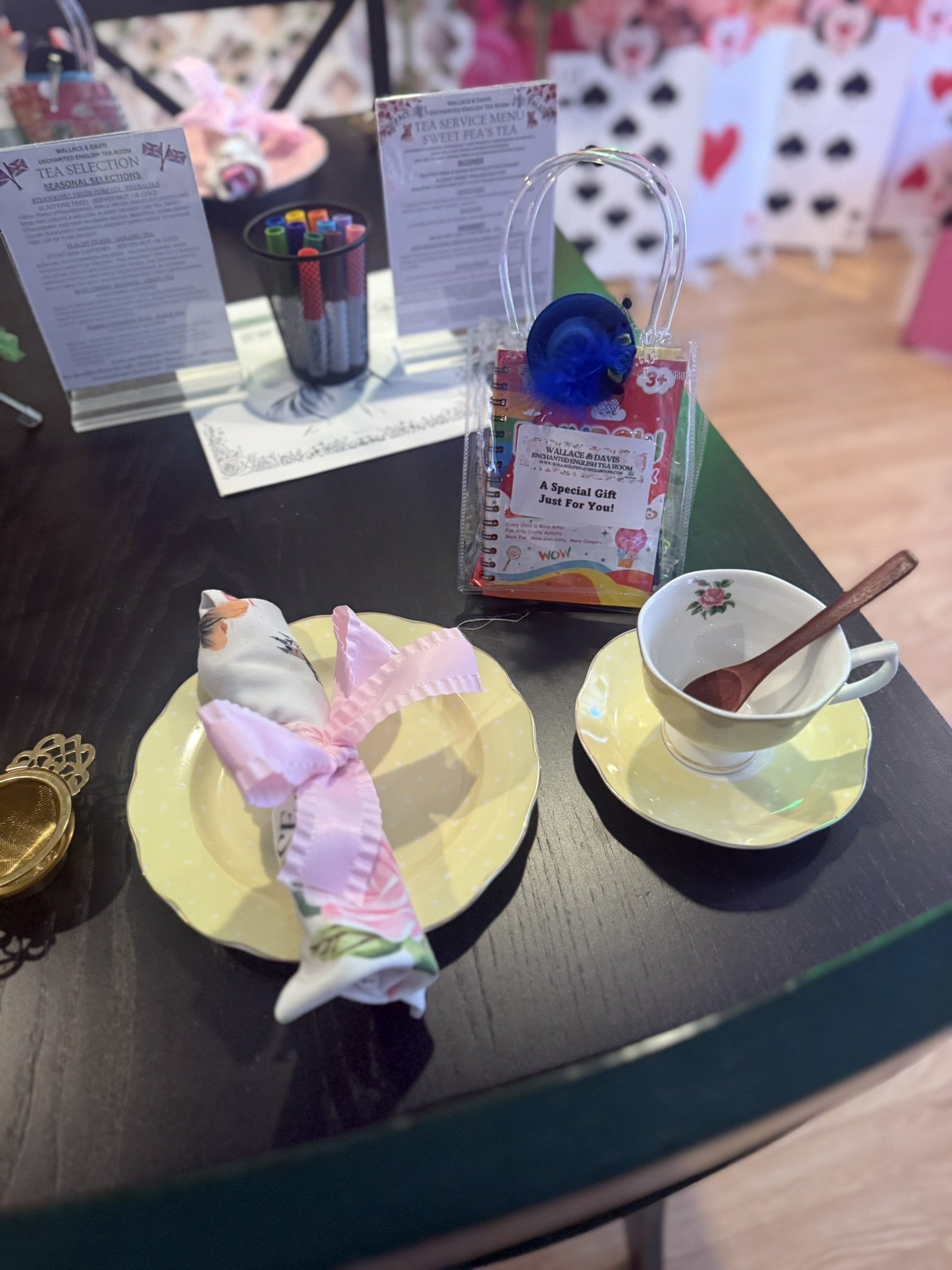 Tea set with tea cup, saucer, and cloth napkin on a dark table, with gifts and informational papers in the background.