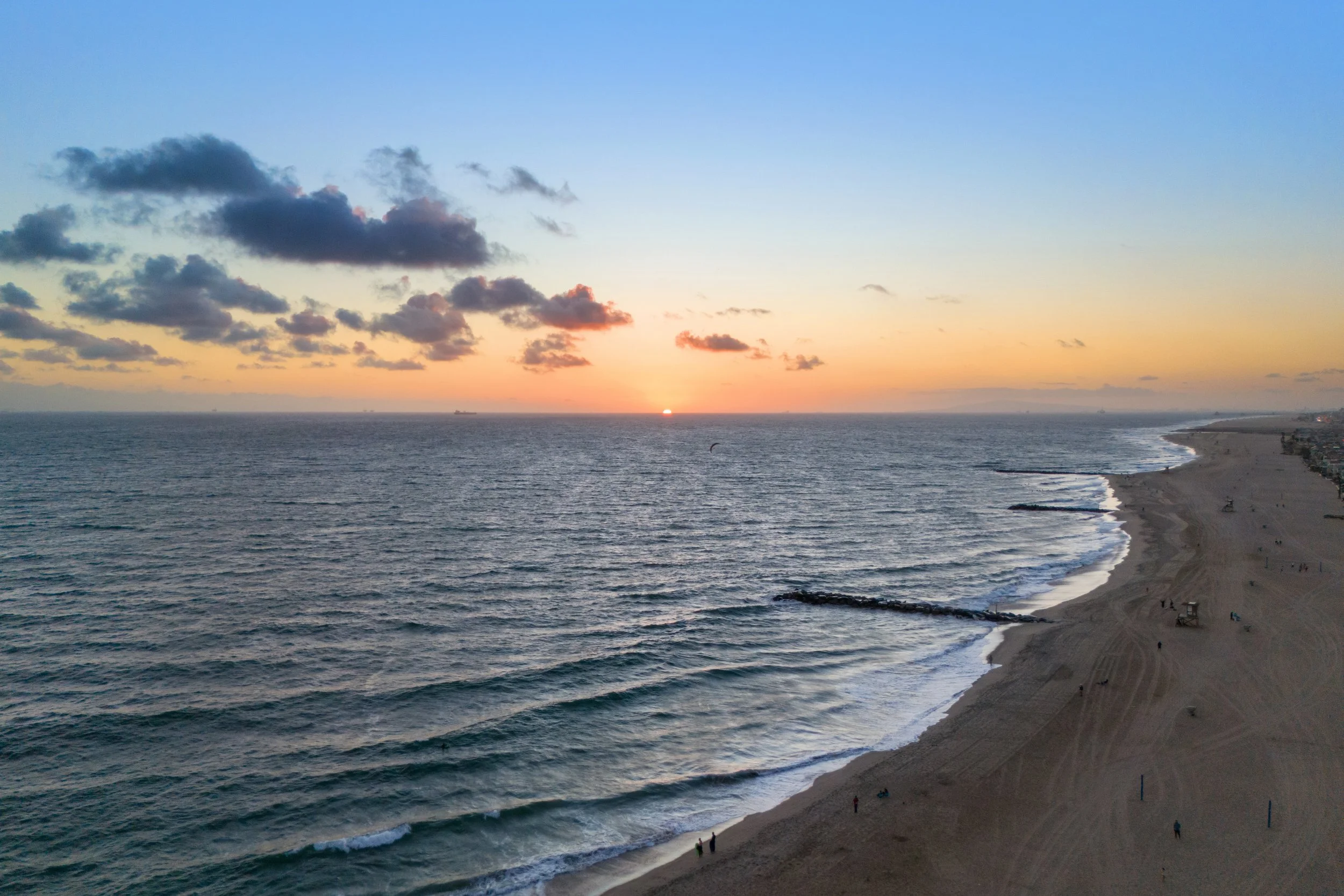 Sunset over the ocean with a sandy beach in the foreground and some clouds in the sky.