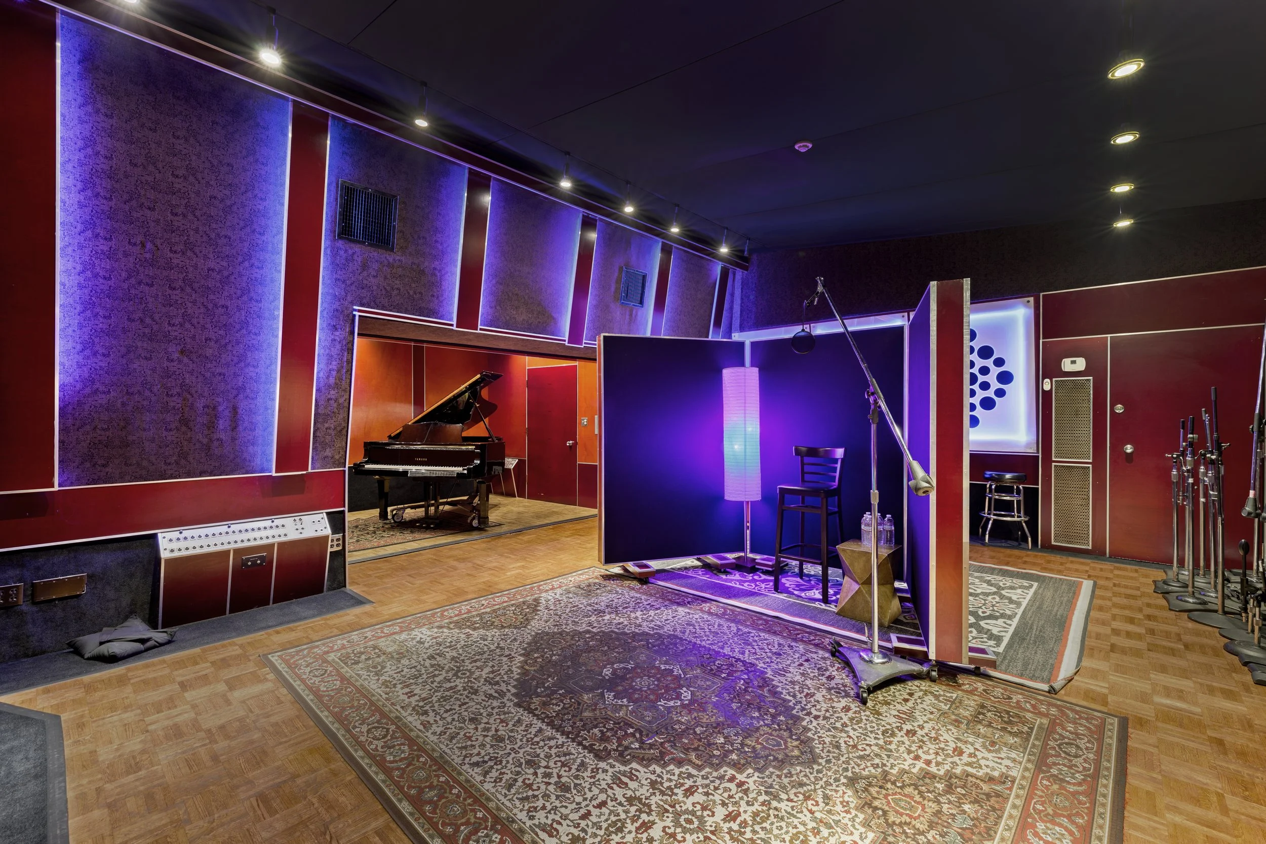 Music recording studio with a grand piano, recording booth, microphone, and soundproof walls with purple and red accents.
