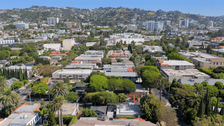 Aerial view of a cityscape showing residential neighborhoods with trees, streets, and taller buildings in the background.