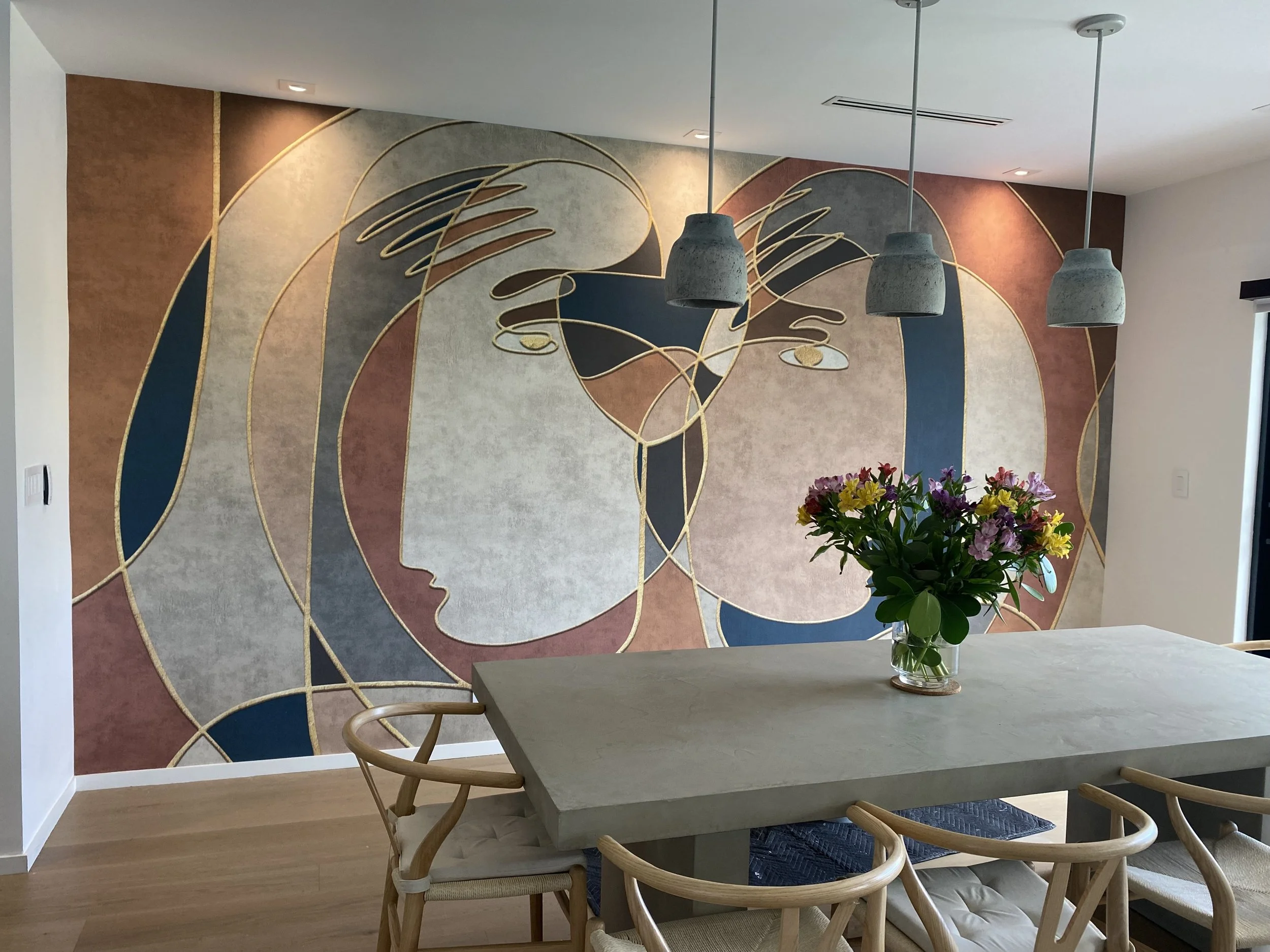 Dining room with modern abstract wall mural, concrete table, wooden chairs, and flower vase centerpiece.