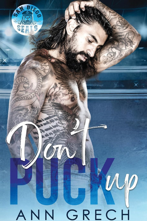 A shirtless man with extensive tattoos on his arms, chest, and torso, standing in a wrestling ring with a serious expression, holding his long hair back, with a San Diego Sea's logo in the background, and a book title "Don't Puck Up" by Ann Grech.