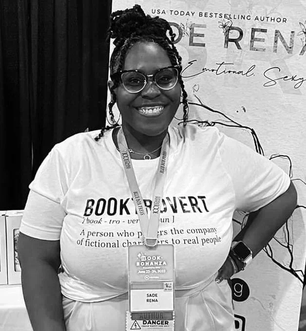 A smiling woman with glasses and braids wearing a BookConza shirt and a conference badge at a book event.