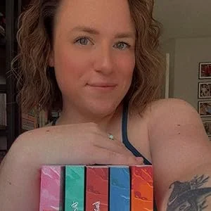 A woman with curly hair holding four colorful books or boxes, smiling at the camera.