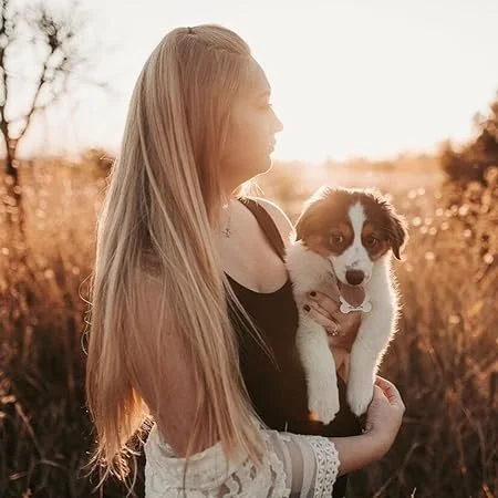 A young woman with long blonde hair holding a small puppy outdoors during sunset.