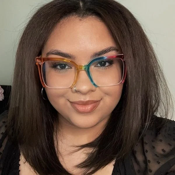 A woman with straight, shoulder-length brown hair, wearing colorful glasses with a rainbow-colored frame, smiling at the camera.
