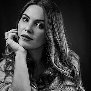 Black and white portrait of a woman with wavy hair, resting her chin on her hand and looking at the camera.