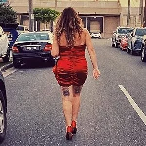 Woman walking away in a red dress and high heels on a city street.