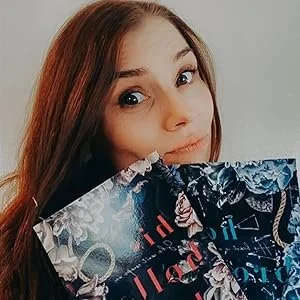 Young woman with long red hair holding a colorful shopping bag, winking at the camera.
