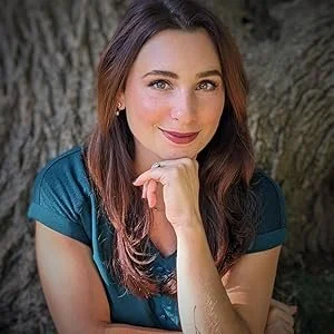 Woman with brown hair, wearing a teal shirt, smiling, outdoors near a tree