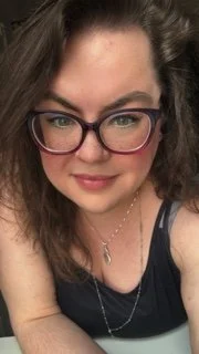 Cartoon woman with long blue hair holding a phone showing a photo of a band.