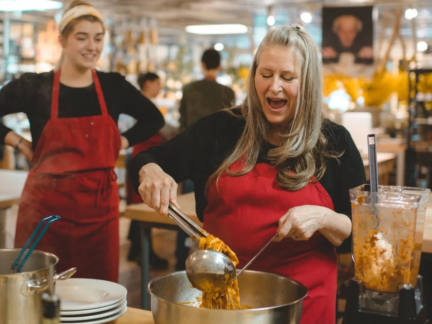 A guest laughing as she stirs fresh pasta into a pan during a class