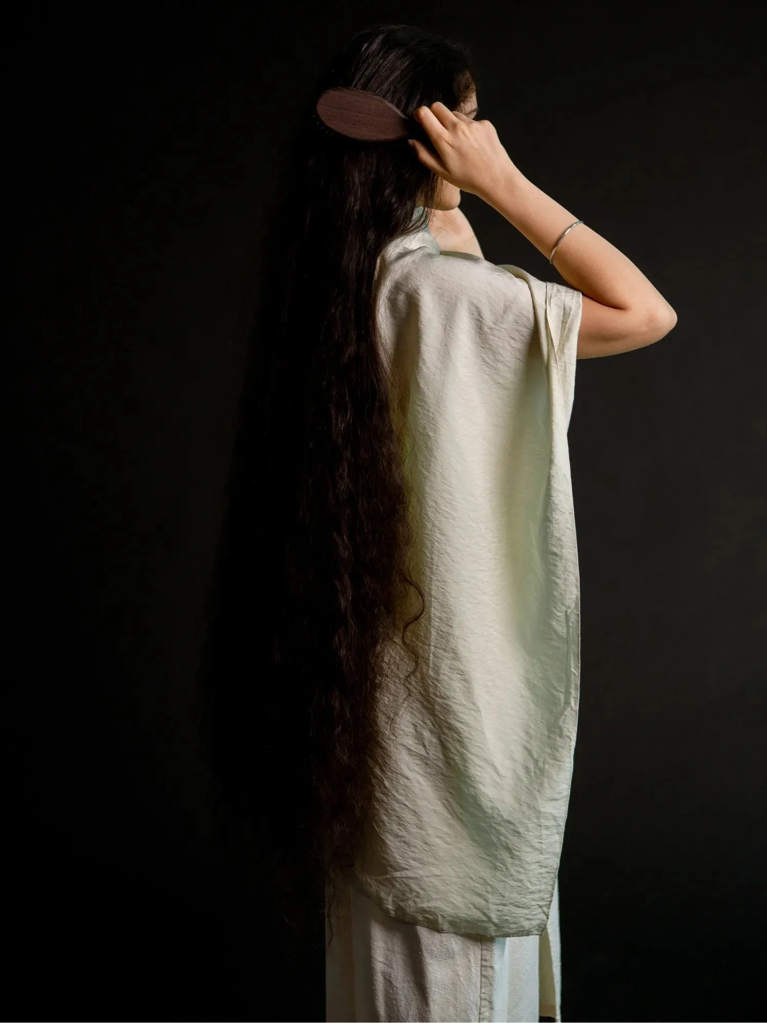 Wooden hair brush in use on long dark hair, back view