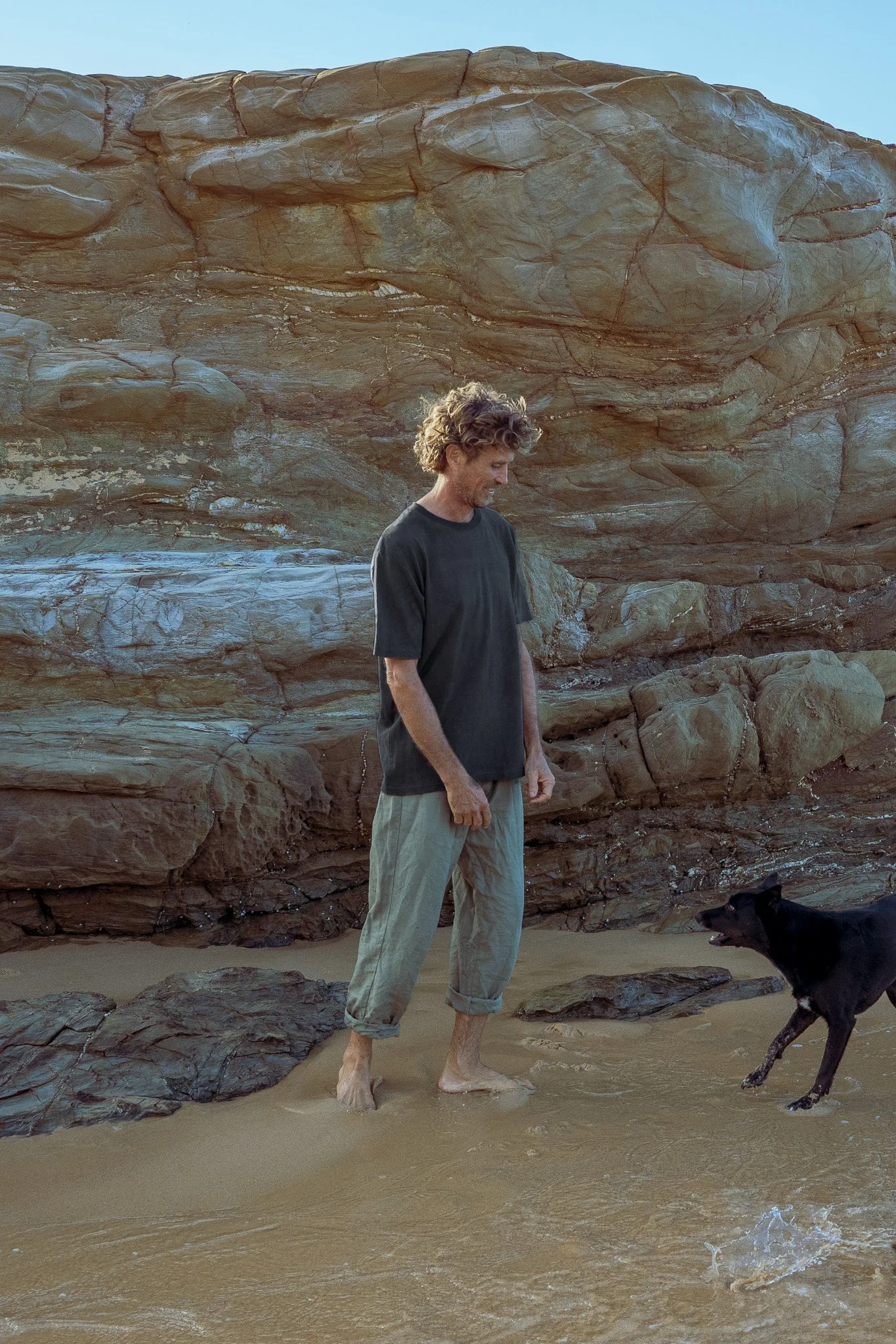 Men's plant dyed hemp tee in indigo and walnut, worn in front of coastal rocks with a dog