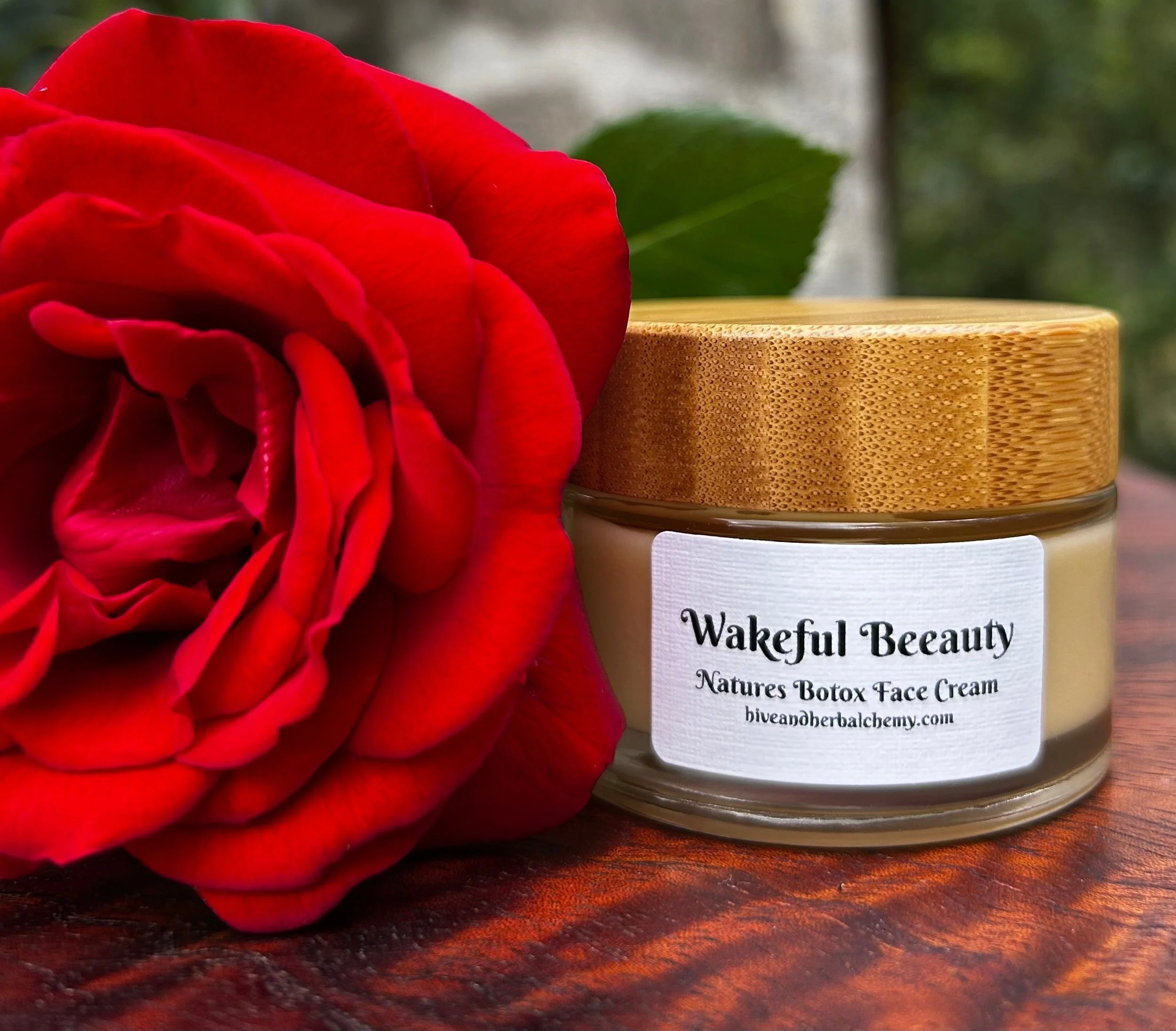 Wakeful Beauty face cream in a glass jar with bamboo lid, beside a red rose