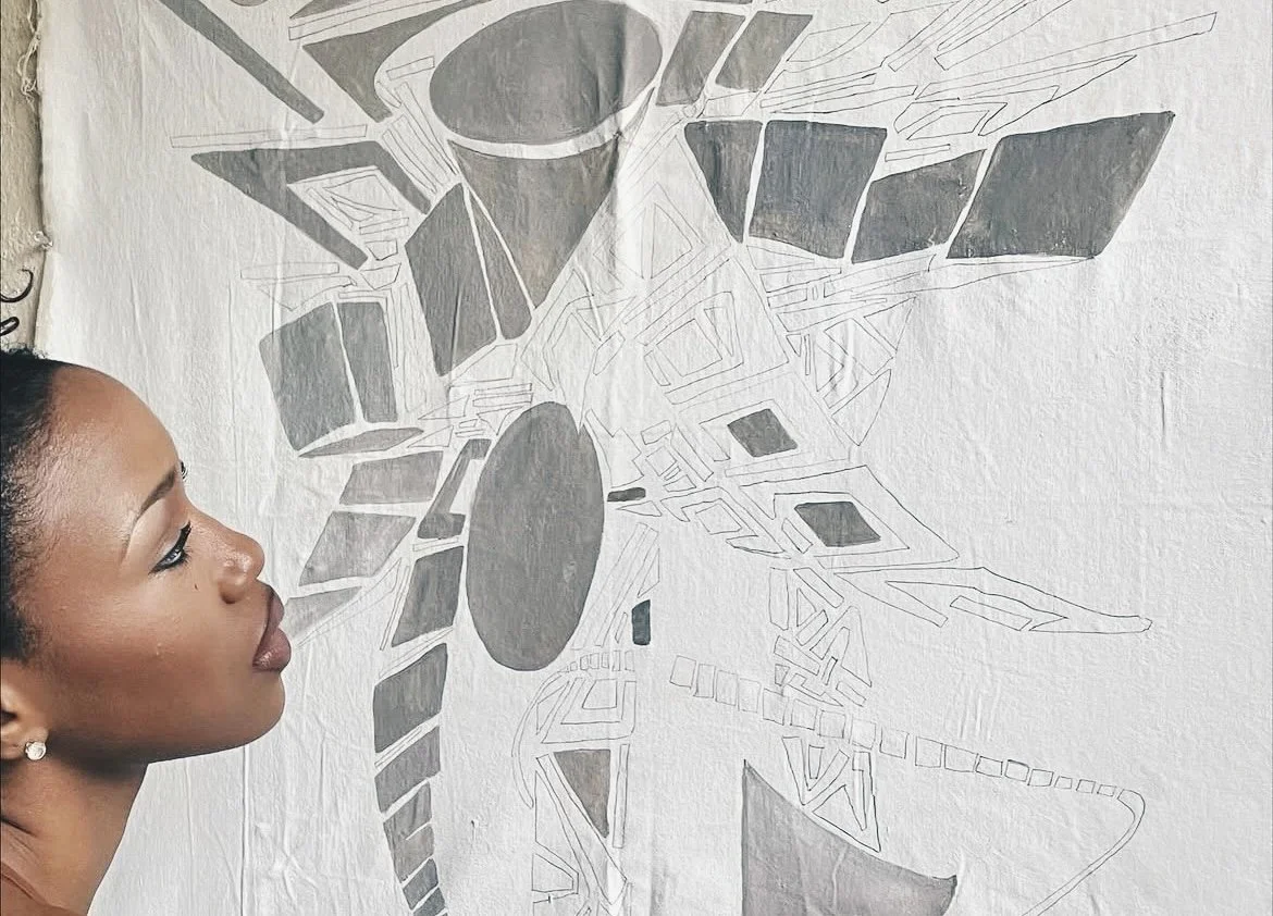 A woman with dark hair and earrings is looking at a large abstract artwork on the wall, which features geometric shapes and patterns in shades of gray.