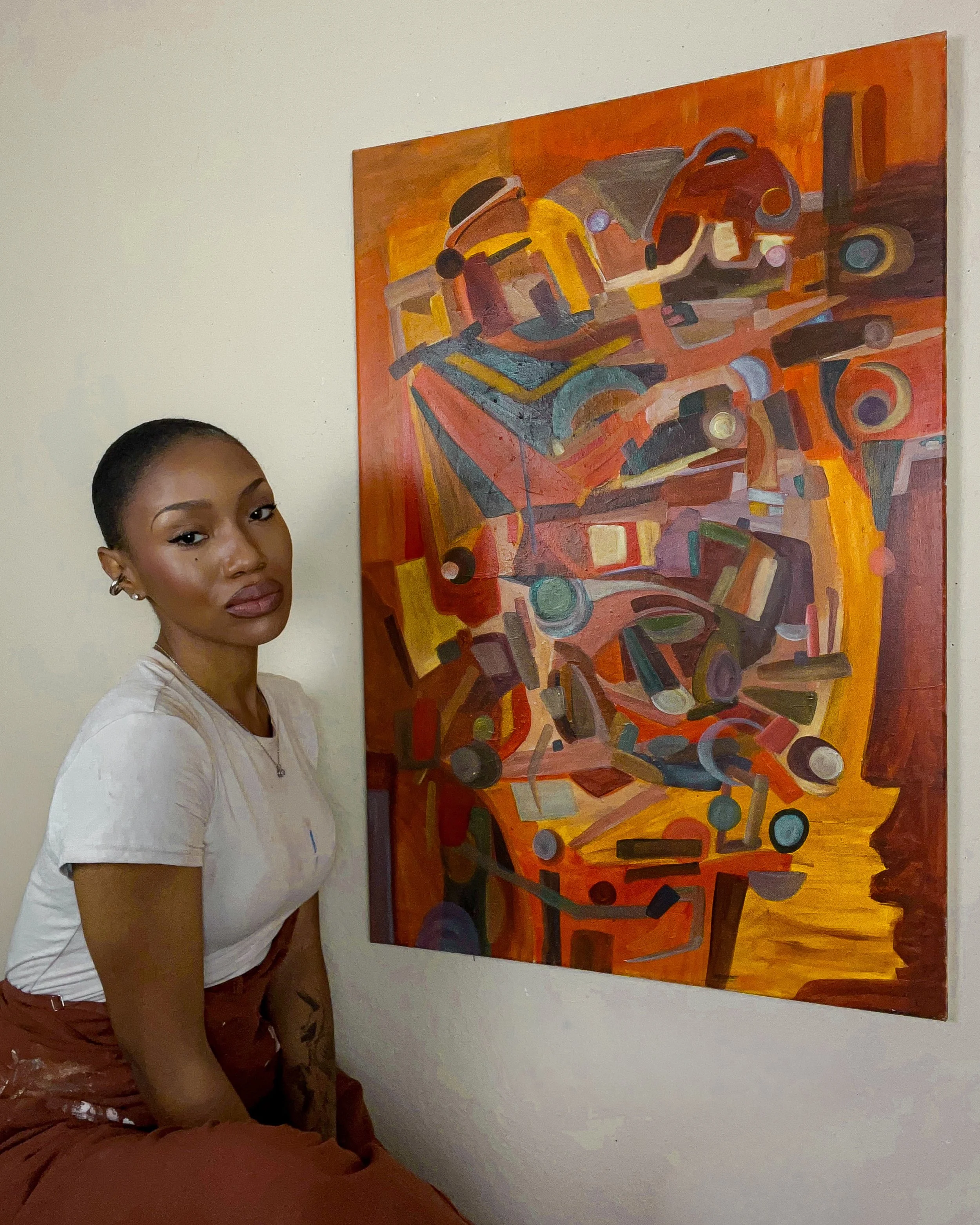 A woman sitting next to an abstract painting featuring various colorful geometric shapes.