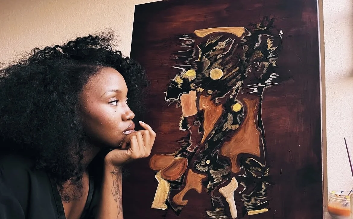 A woman with curly black hair looking thoughtfully at an abstract painting of a woman with gold earrings and dark hair.