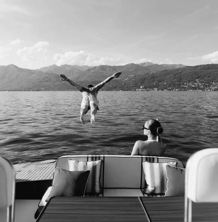Black and white photo of a man jumping out of a boat and a woman on the boat