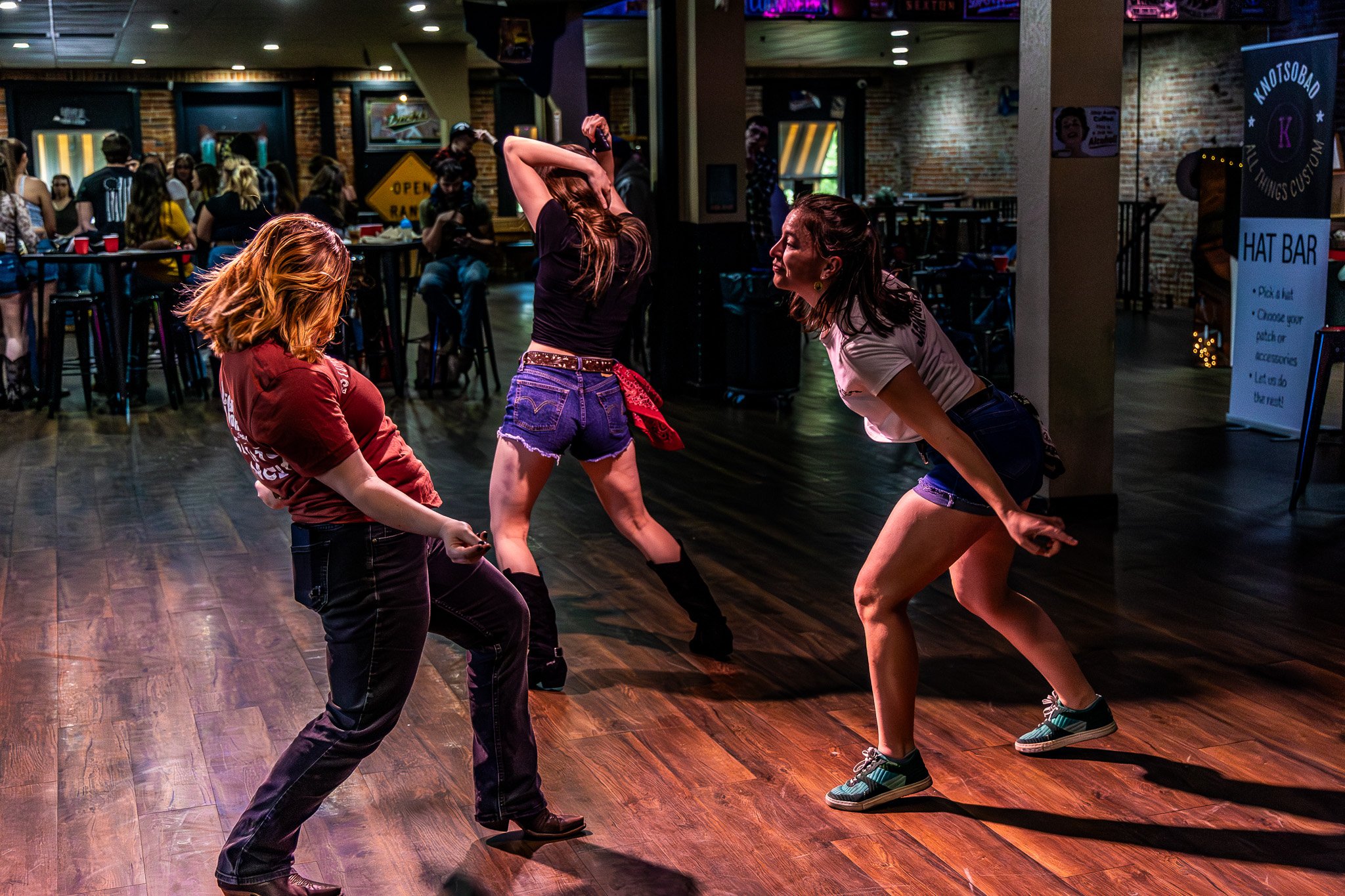 Three women dancing energetically in a bar with other patrons watching.