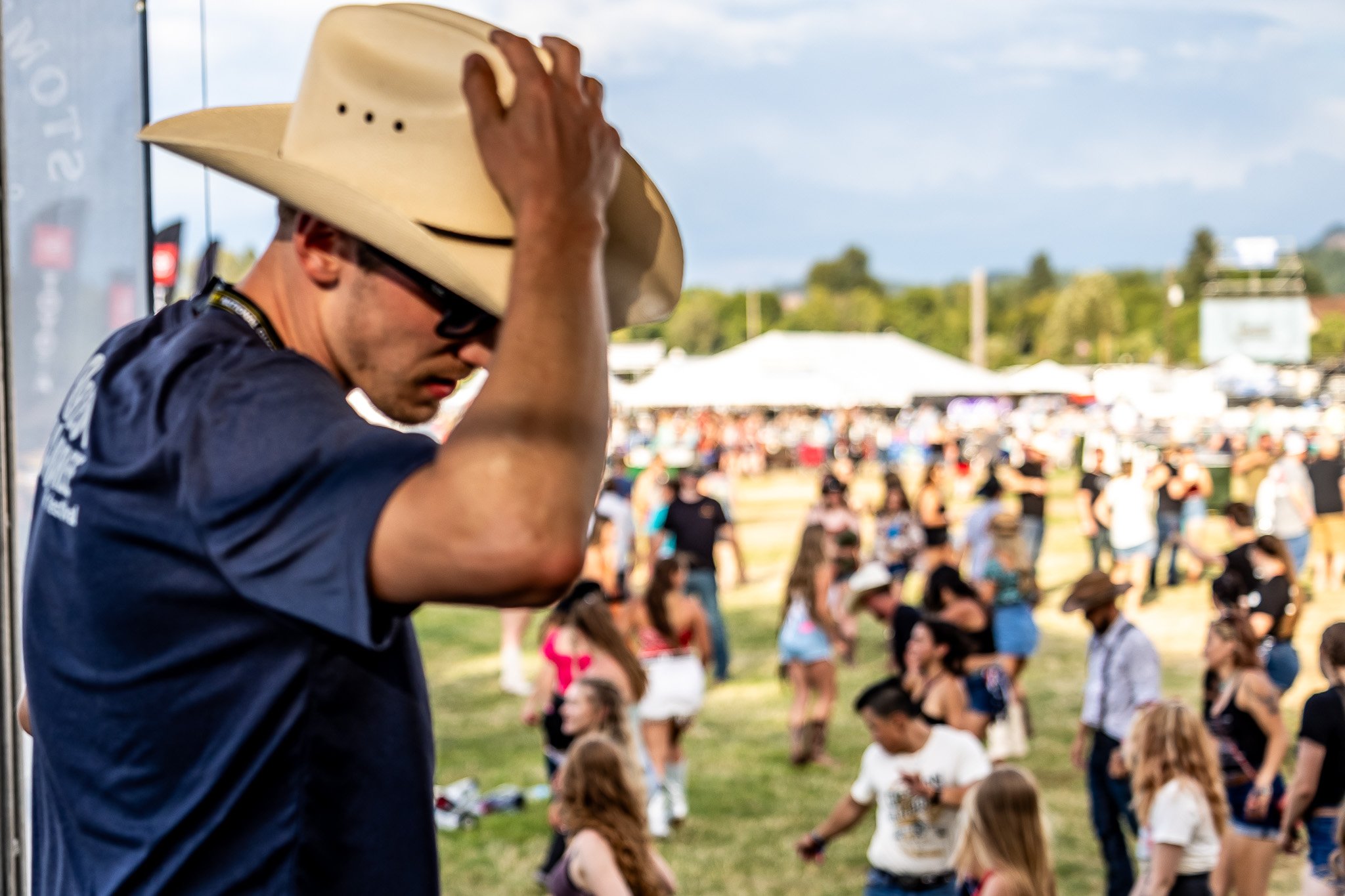 Man in cowboy hat at outdoor event with crowd in the background