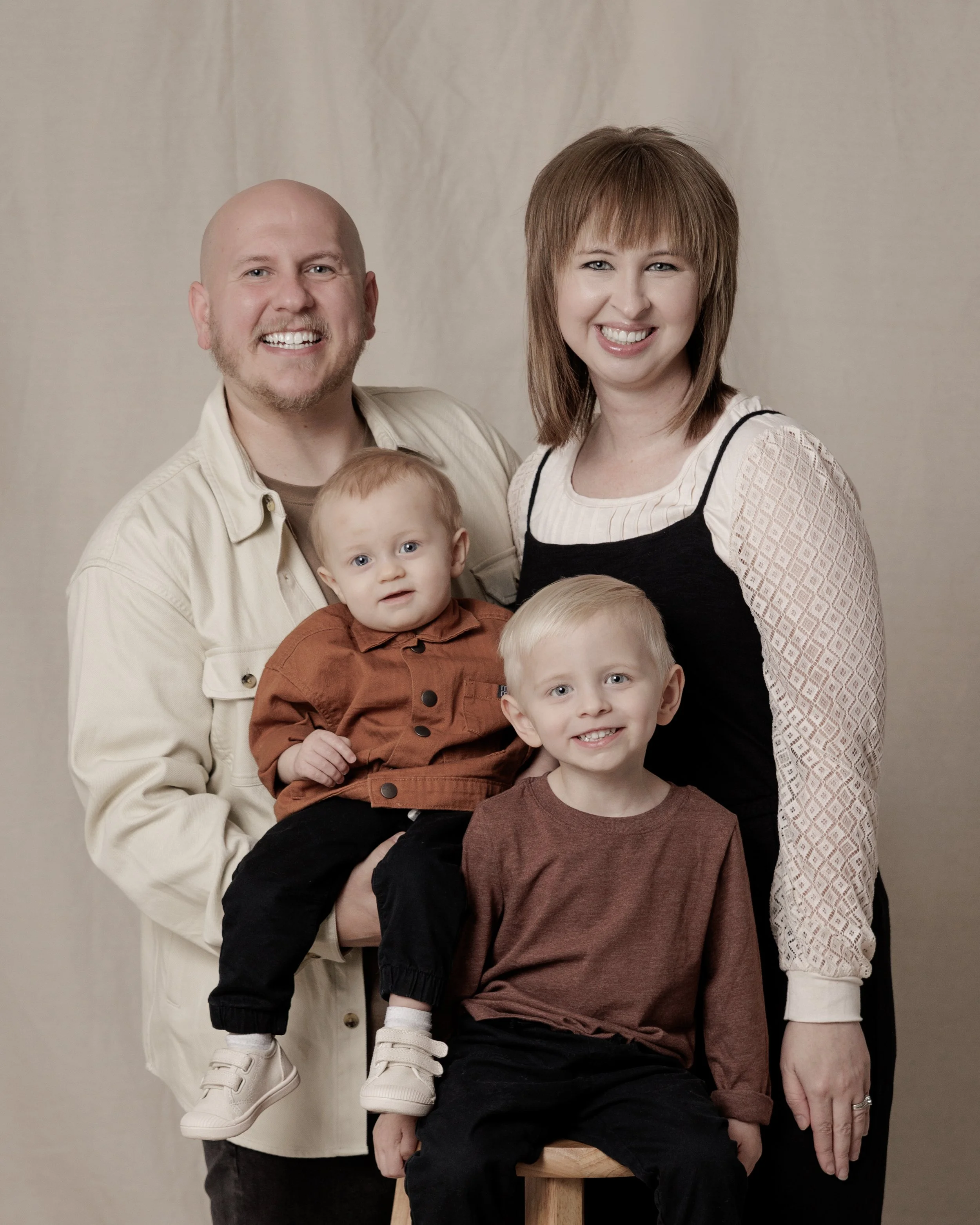 A family of five posing together indoors, consisting of a father, mother, and three young children, all smiling.