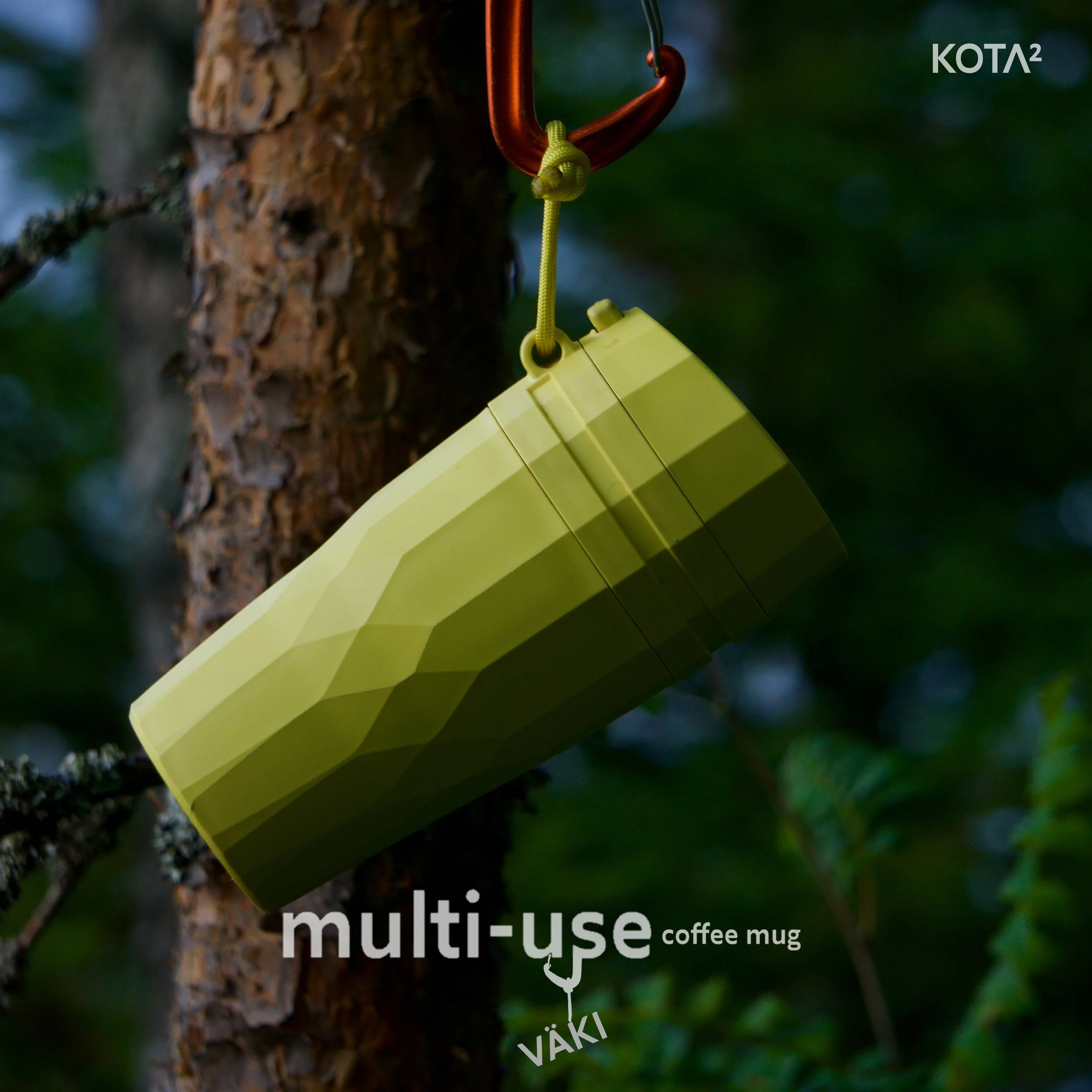 A yellow multi-use coffee mug hanging from a tree branch with a green carabiner clip, surrounded by green foliage.
