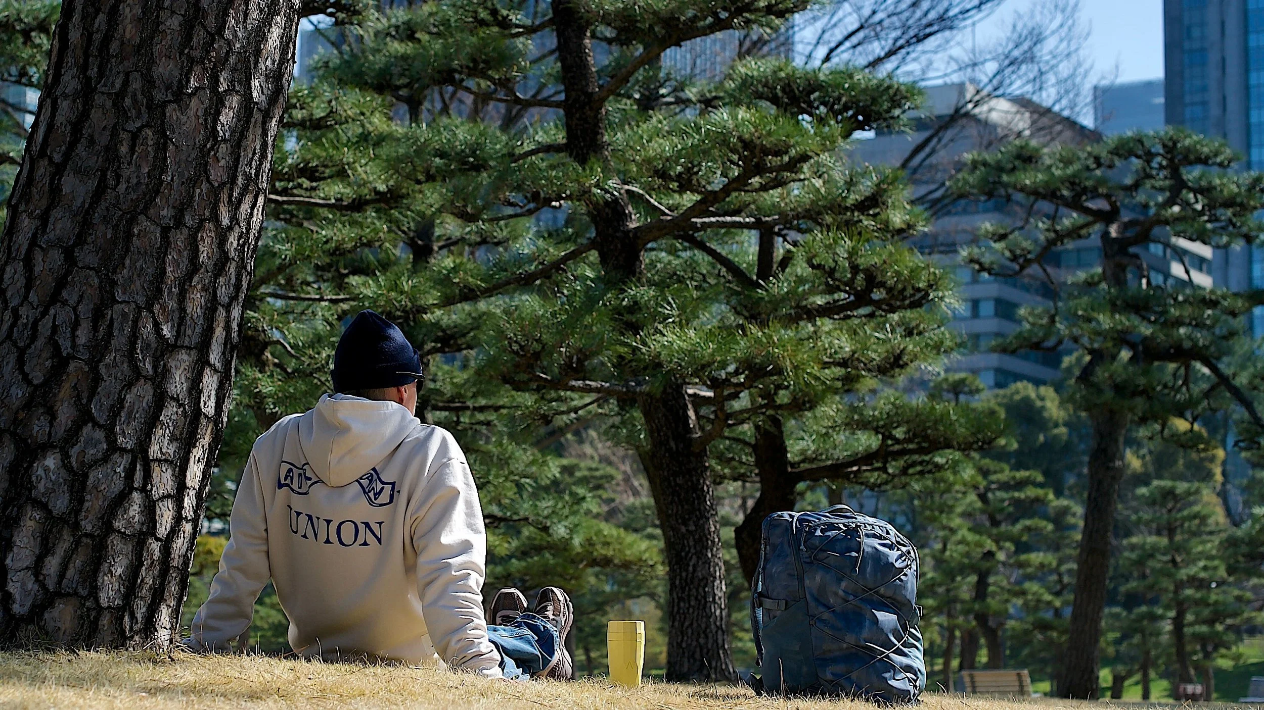 Väki keltainen Tokio istuu reppu selässä puistossa 16:9.jpeg