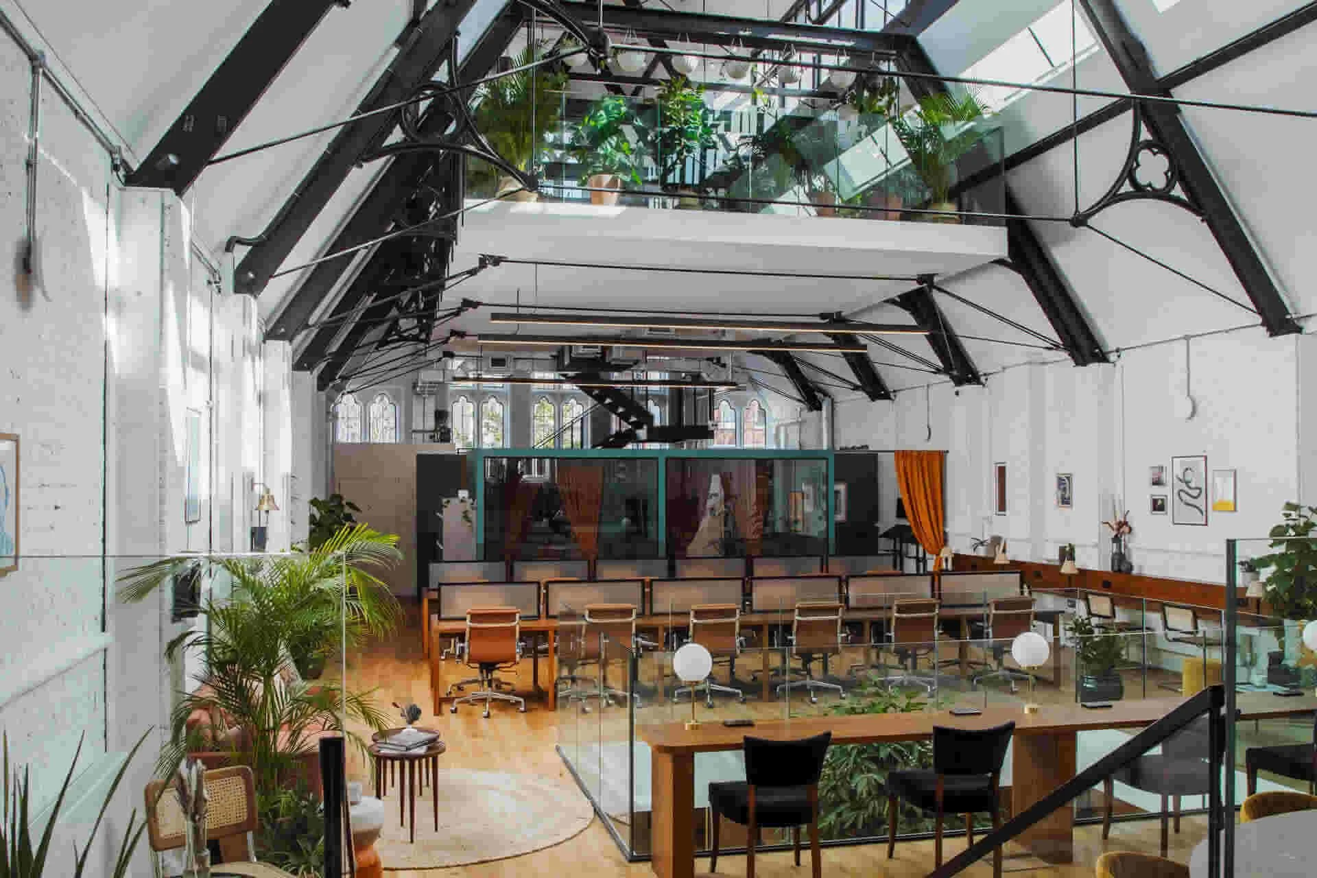 Interior of a modern office space with high ceilings, large windows, and multiple levels with glass railings, plants, and contemporary furniture.