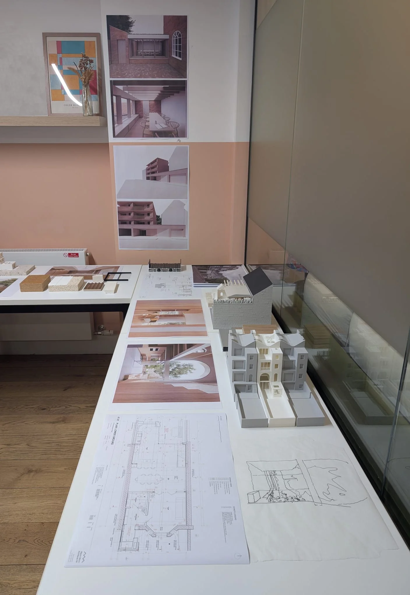 Architectural models, blueprints, and design images of a building project displayed on a white table in an office or studio.