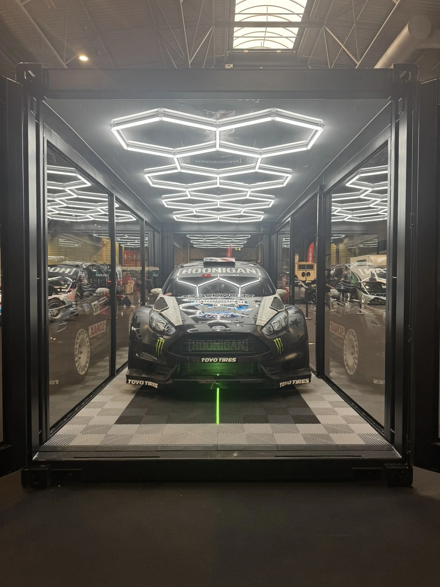 A display of a racing car inside a glass-enclosed space with geometric LED lighting on the ceiling.