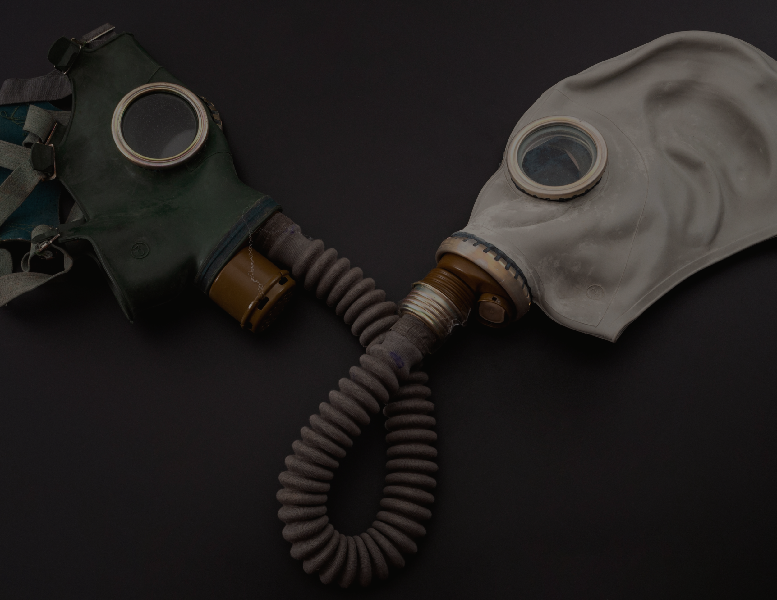 Two vintage gas masks on a dark background, connected by a hose.